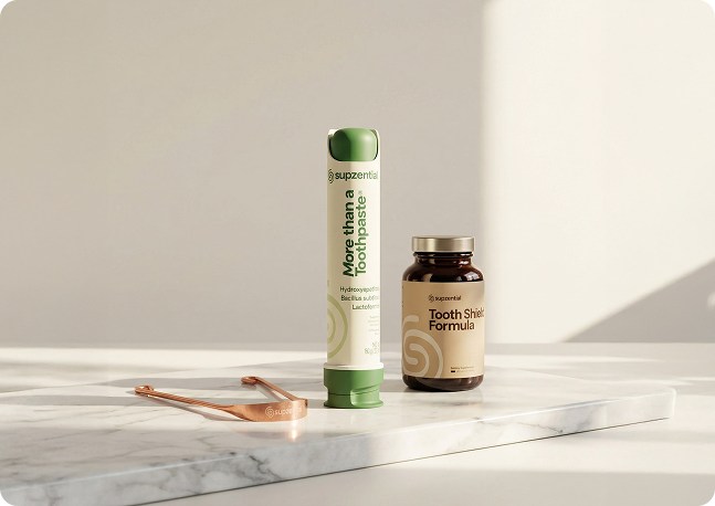 A minimalist display of Supzential oral care products including More than a Toothpaste, Tooth Shield Formula, and a copper tongue scraper on a marble surface.